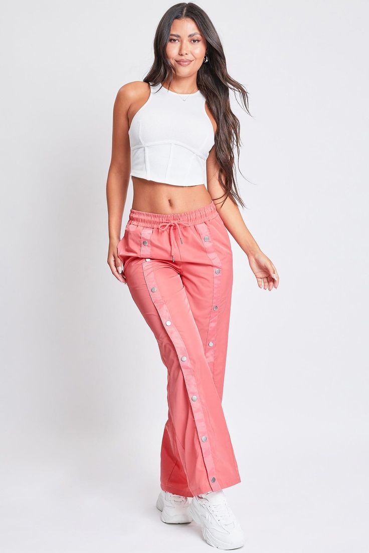 Off-duty vibes! Our Snap Wide Leg Pant is the perfect combination of parachute pants and track pants. These are great for days you want to rock a comfy and sporty look, but with a streetwear vibe. Featuring snap buttons centered along the fronts and backs of each leg for design and functional purposes. Not only do they look super trendy and chic, but you can unsnap or snap them to adjust the pants to the width of your liking. Also designed with an elastic waistband and drawstring for ultimate co Trendy Streetwear Parachute Pants With Elastic Waistband, Trendy Parachute Pants For Streetwear, Trendy Sports Pants, Summer Streetwear Sweatpants With Cargo Pockets, Summer Cargo Sweatpants For Streetwear, Trendy Wide Leg Sports Pants, Spring Streetwear Hip Hop Parachute Pants, Spring Hip Hop Parachute Pants For Streetwear, Hip Hop Parachute Pants For Spring Streetwear