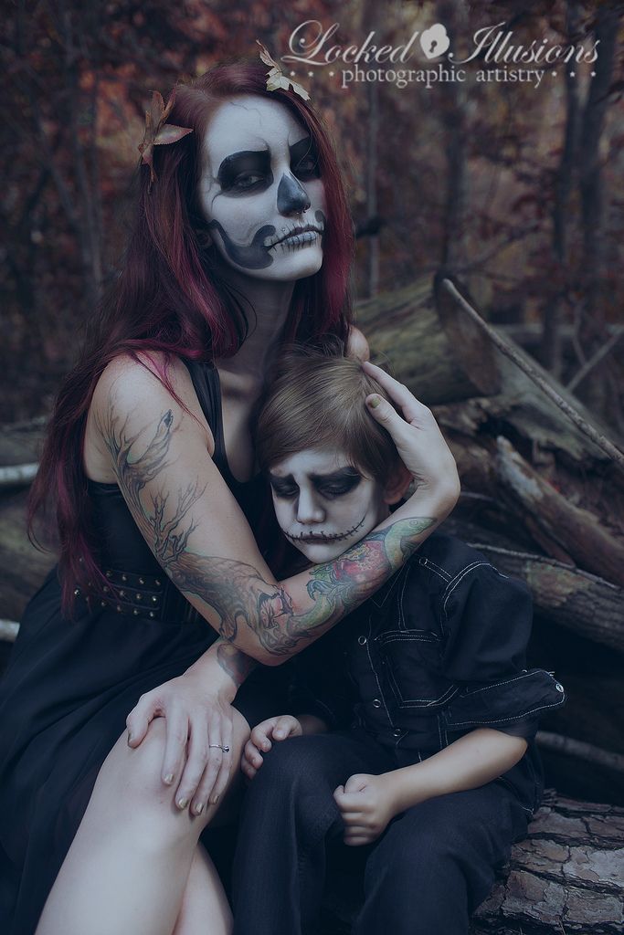 a woman and child dressed up in skeleton makeup sitting on a log with their arms around each other