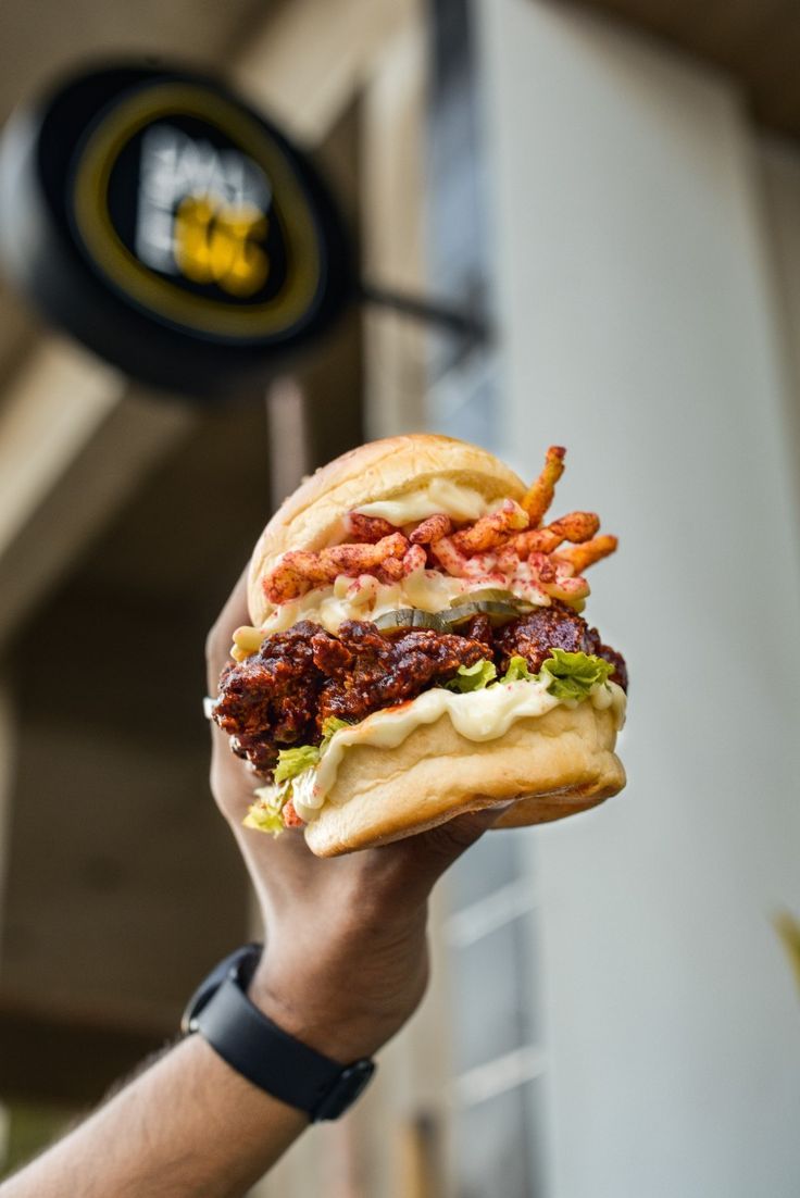 a person holding up a large sandwich with meat and lettuce on it in front of a building