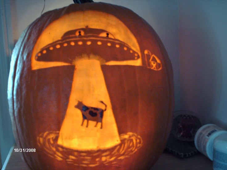 a pumpkin carved to look like an alien ship with a cow on it's head