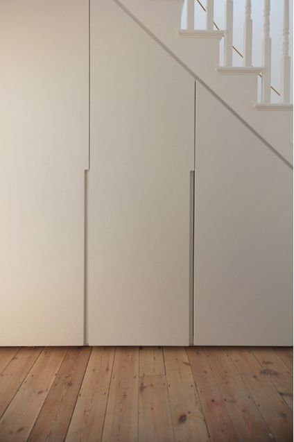 an empty room with white walls and wooden floors, next to a stair case in the background