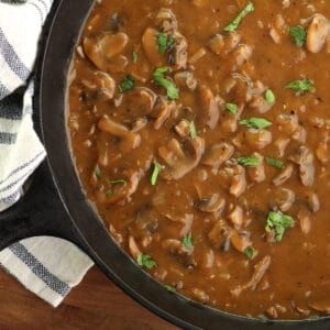 a skillet filled with mushroom stew on top of a wooden table