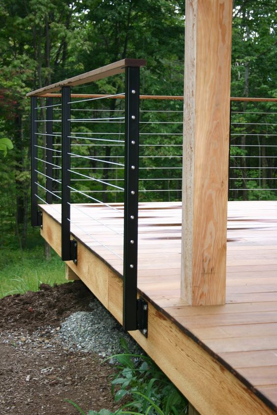 a wooden deck with metal railings in the middle of trees and grass around it