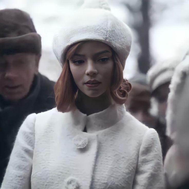 a woman with red hair wearing a white coat and hat while standing next to other people