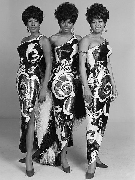 three women standing next to each other wearing dresses with designs on them and feathers in their hair