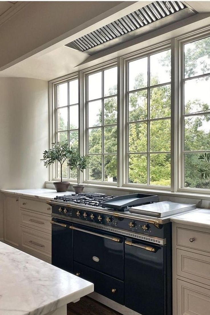 a kitchen with an oven, stove and counter tops in front of two large windows