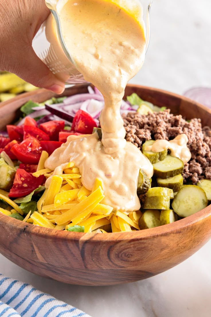 a person pouring dressing over a salad in a wooden bowl