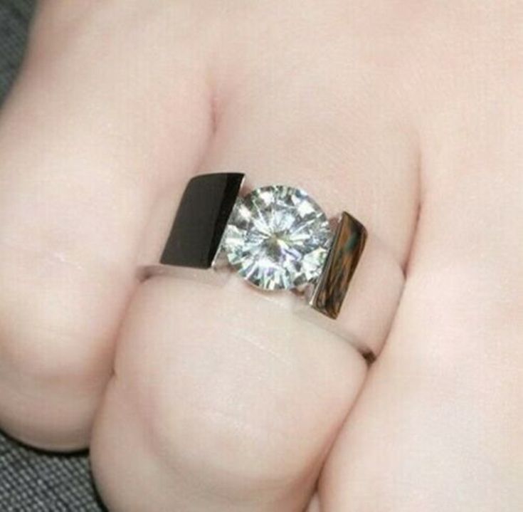 a close up of a person's hand holding a ring with a diamond on it