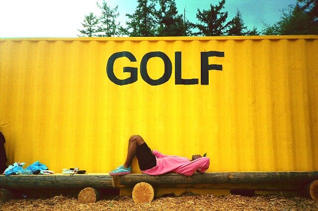 a person laying on top of a wooden bench next to a yellow container with the word golf written on it