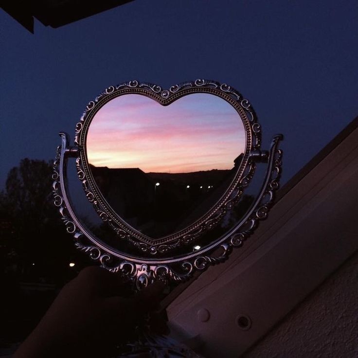 a heart shaped mirror sitting on top of a window sill in the night sky