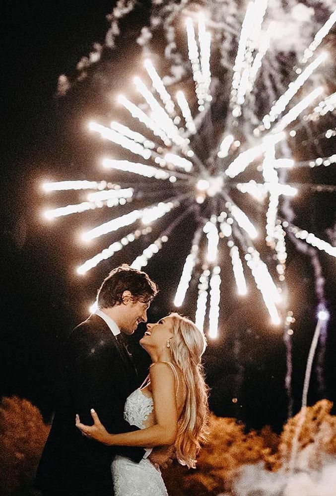 a bride and groom standing in front of fireworks at night with their faces close to each other