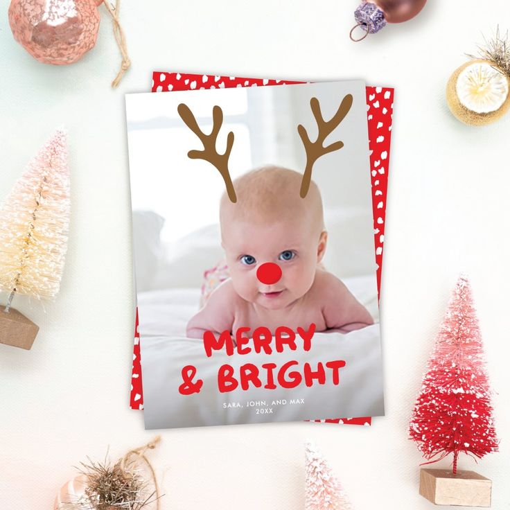 a christmas card with a photo of a baby wearing reindeer antlers on it, surrounded by other holiday decorations