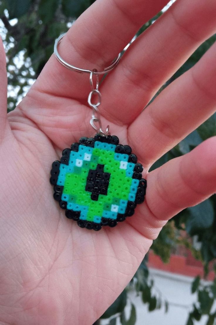 a hand holding a green and black beaded keychain in it's palm