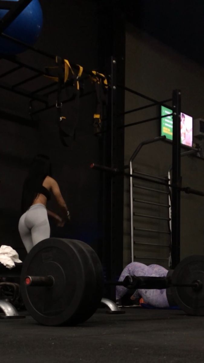 a woman squats on the ground with a barbell in front of her and another person behind her