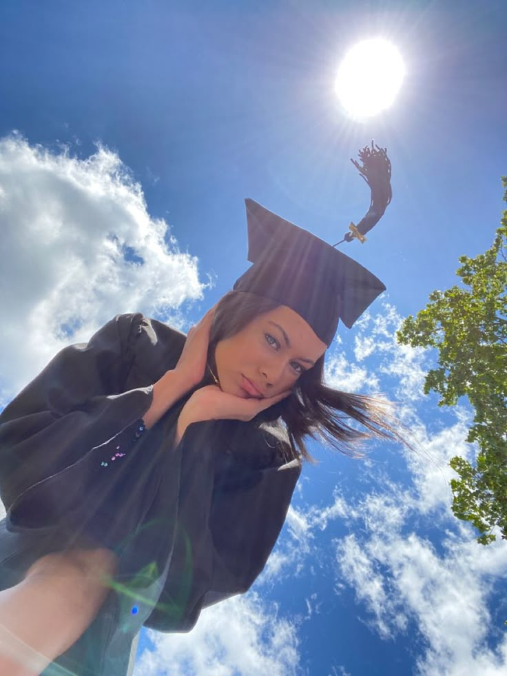 a young woman wearing a graduation cap and gown standing in front of a blue sky