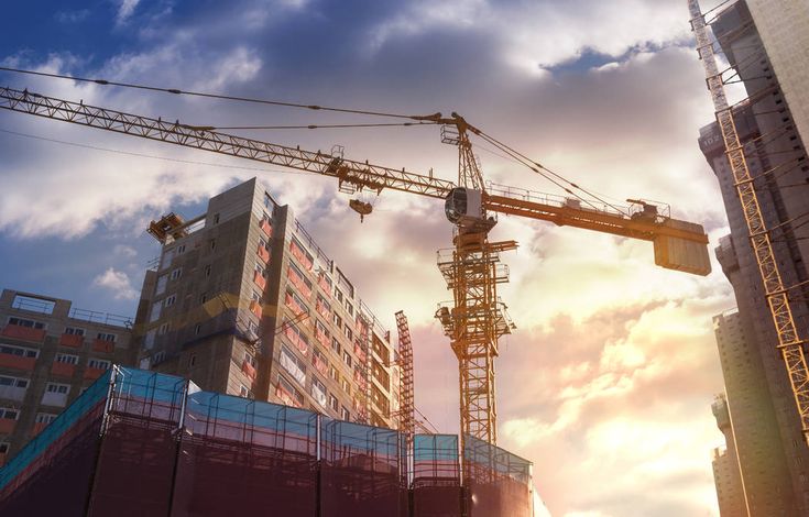 the sun is setting behind construction cranes in front of tall buildings on a city street