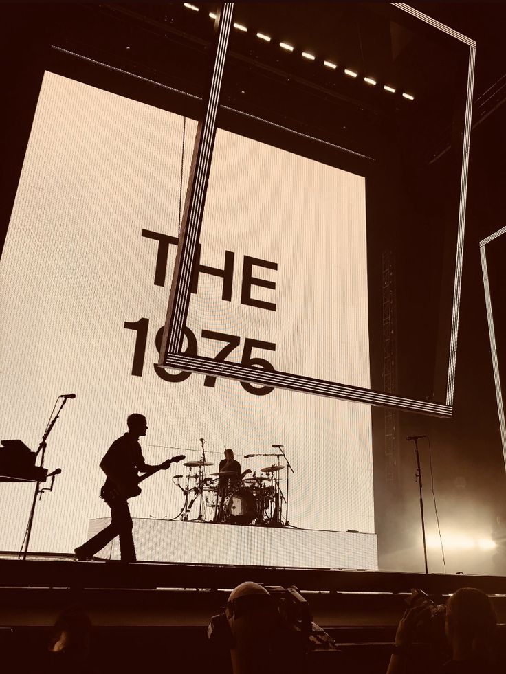 the silhouette of a man playing guitar in front of a large screen that says the 1 / 2 / 4