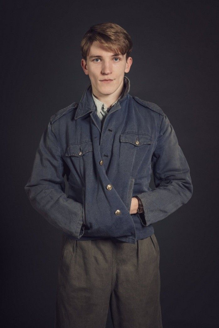 a young man wearing a jacket and tie standing in front of a black background with his hands on his hips