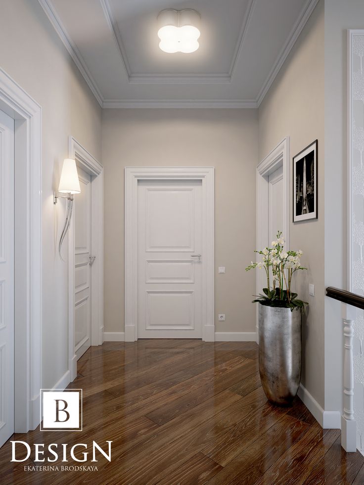 an empty hallway with wooden floors and white walls, along with a metal planter filled with flowers