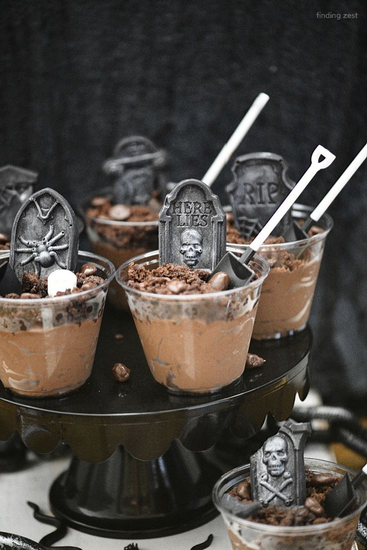 halloween desserts in plastic cups with skeleton heads and tombstones on top, sitting on a black cake stand