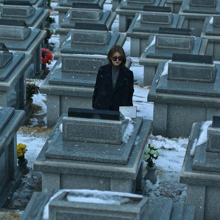 a woman standing in the middle of a cemetery filled with headstones and flowers