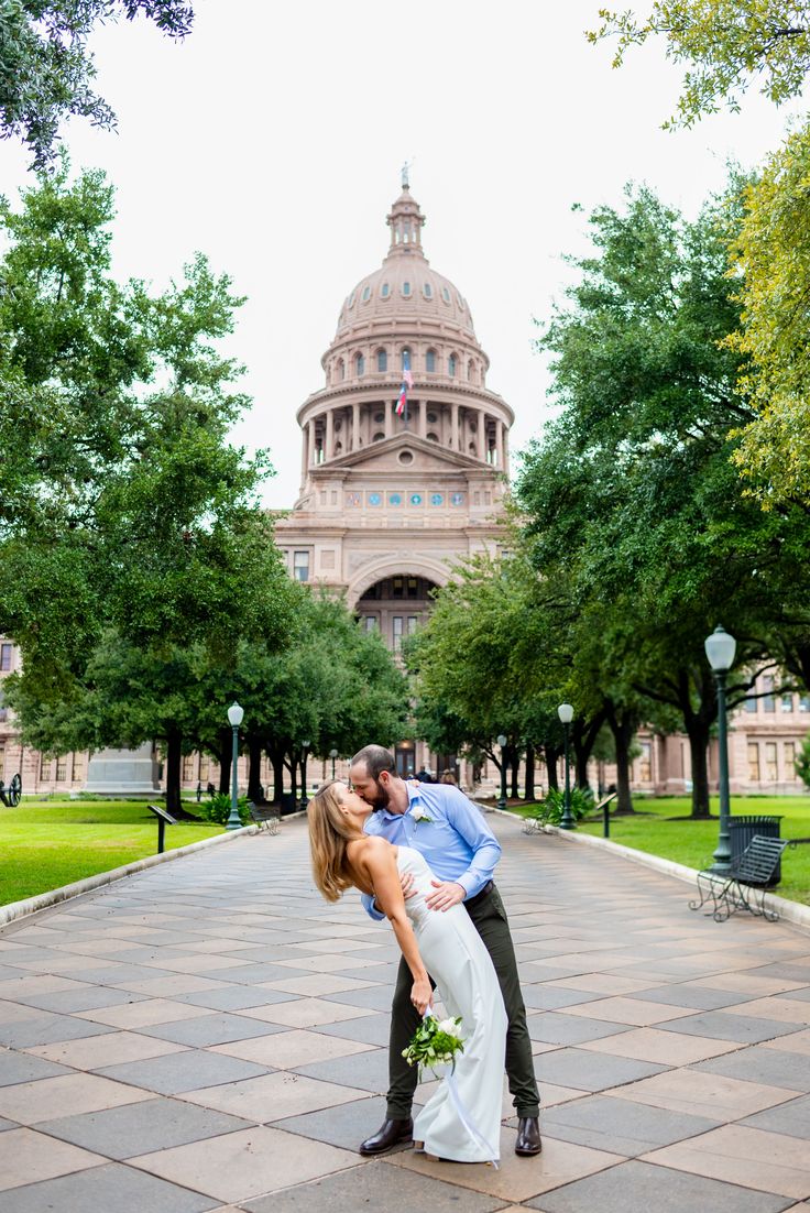 a bride and groom kissing in front of the state capitol building