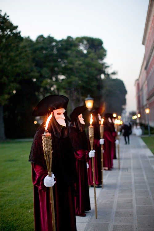 a row of people dressed in long gowns and holding torches on the side of a sidewalk