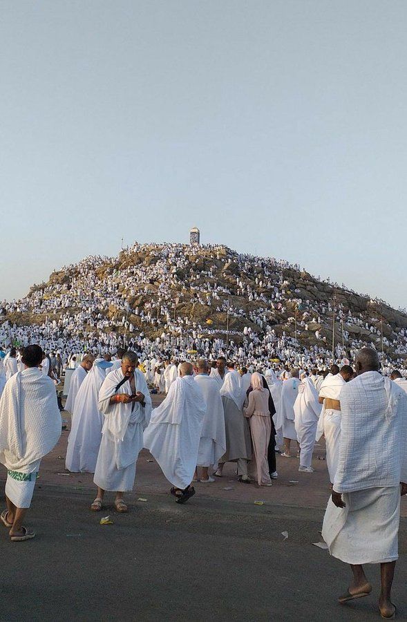 a group of people dressed in white walking down a street next to a large hill