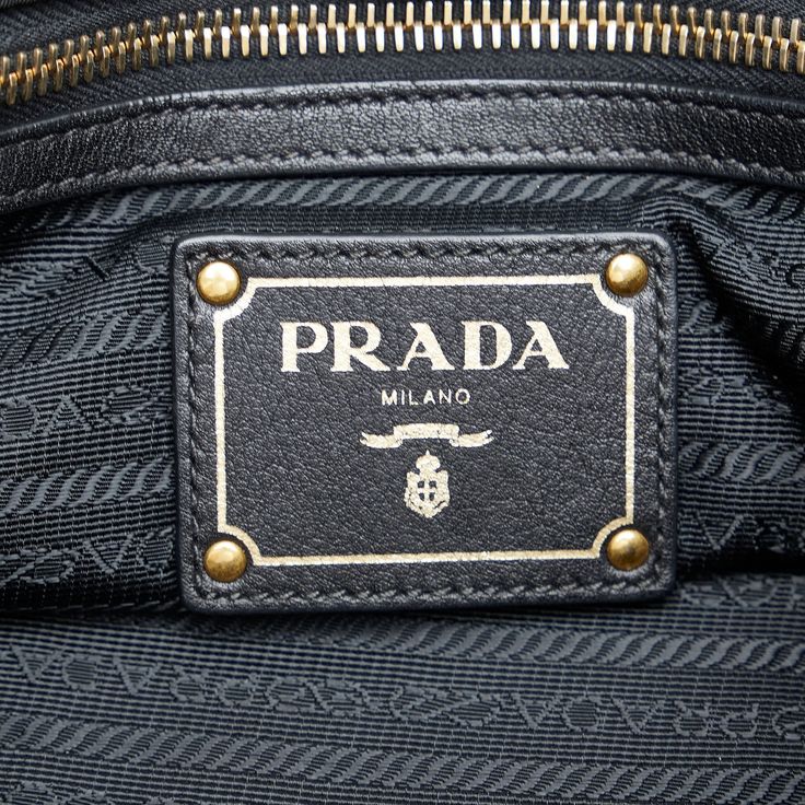 This Prada TessuTo handbag is made of black nylon canvas and has rolled leather indexes. The Bag is also decorated with gold -colored details. A golden Prada lettering shines on the front. The Bag Has a magnetic closure at the upper opening. Inside the Bag there are a zipper compartment and a slide compartment. The Bag can be in the hand or with a removable leather shoulder strap over the shoulder. Leather Bags With Gold-tone Logo Plaque And Double Handle, Leather Bags With Double Handle And Gold-tone Logo, Black Leather Bags With Logo Plaque, Gold Bag With Gold-tone Logo Plaque And Double Handle, Gold Shoulder Bag With Logo Plaque For Everyday, Luxury Shoulder Bag With Logo Plaque And Top Handle, Business Shoulder Bag With Gold-tone Logo Plaque, Luxury Shoulder Bag With Top Handle And Logo Plaque, Leather Shoulder Bag With Logo Plaque For Travel