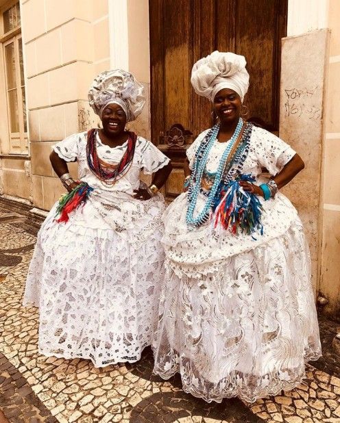 two women in white dresses standing next to each other on a cobblestone street