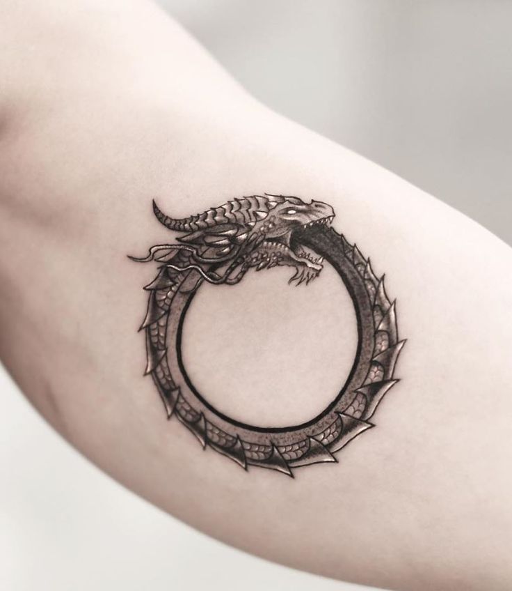 a black and white photo of a dragon in a circle tattoo on the right arm