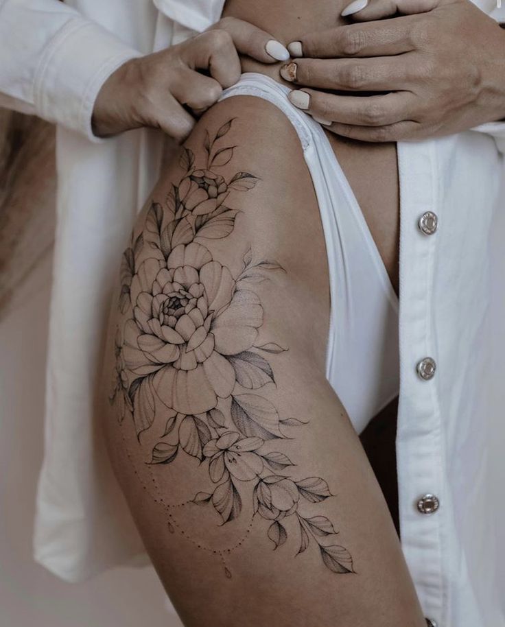 a woman's thigh with flowers on it and her hands behind her back, while she is showing off her tattoo