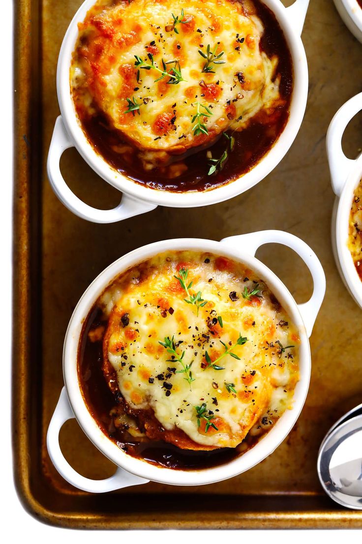 four white bowls filled with food on top of a metal tray next to silver spoons