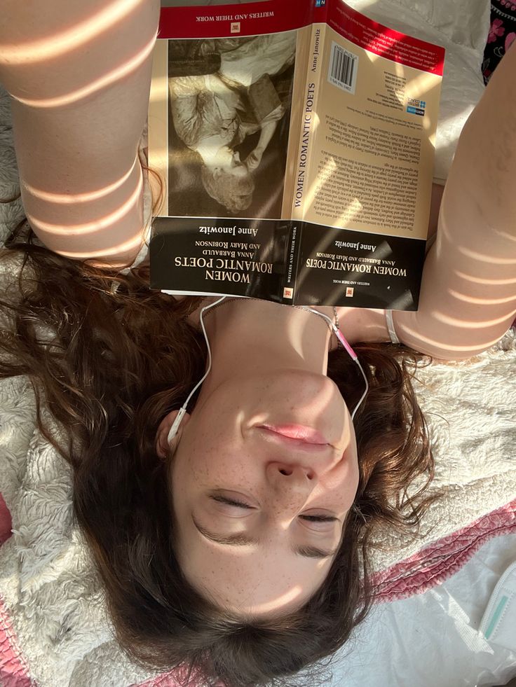 a woman laying on top of a bed with a book in her hand over her head