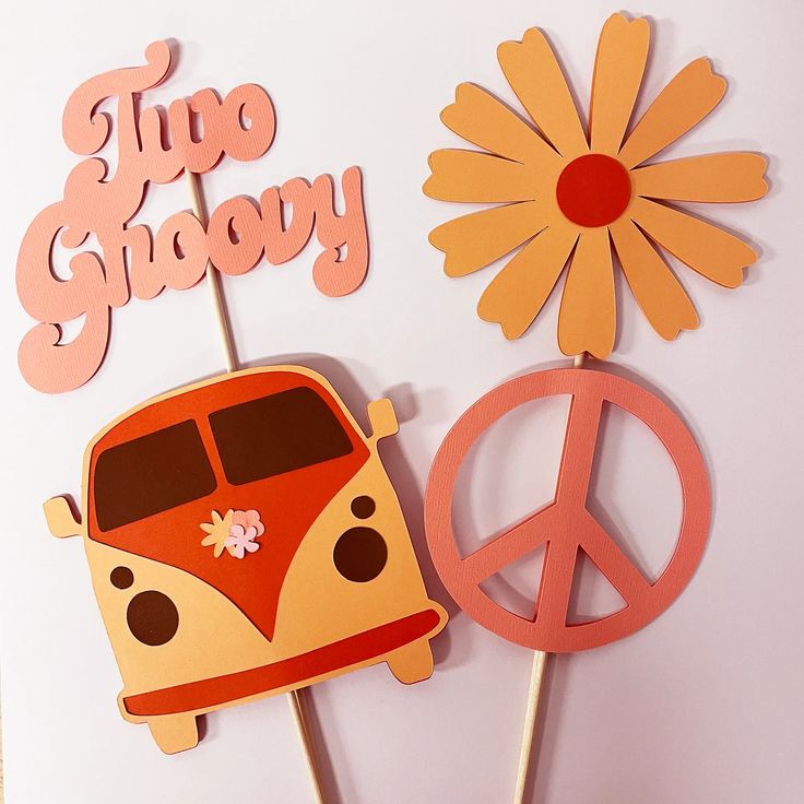 there are two cupcake toppers with flowers and a bus on them, one has peace signs