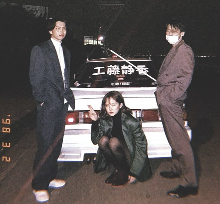 two men and a woman standing next to a car