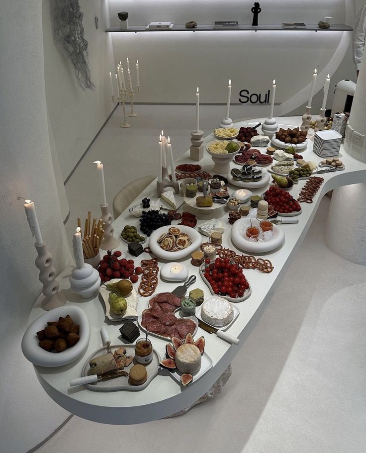 a table filled with lots of food on top of a white counter next to candles