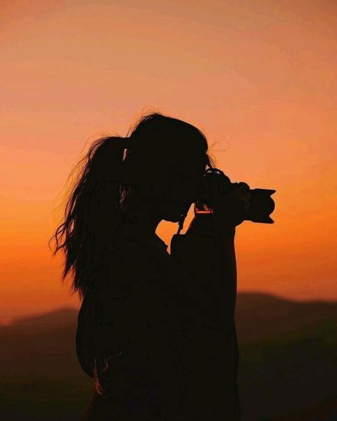 the silhouette of a woman holding a camera up to her face as the sun sets