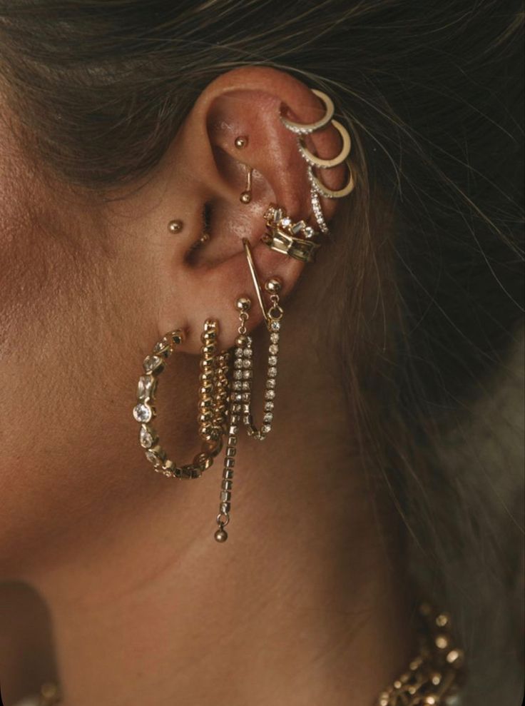 a close up of a person with ear piercings on their ears and wearing gold jewelry