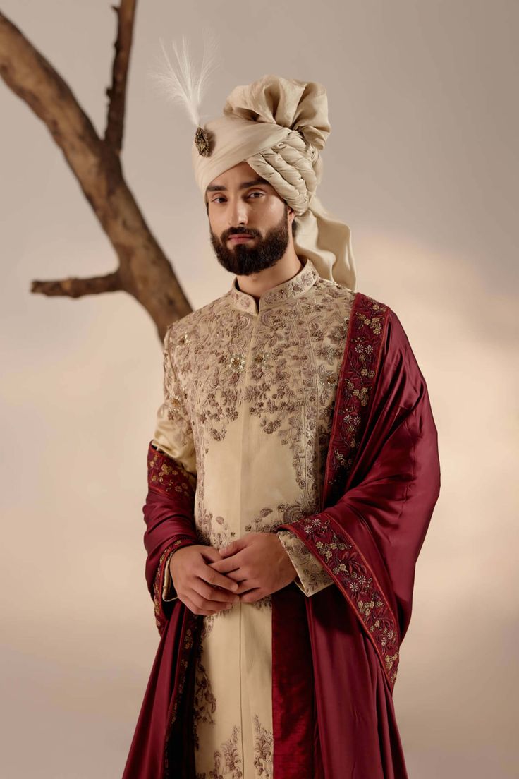 a man with a turban standing in front of a tree wearing a red and white outfit