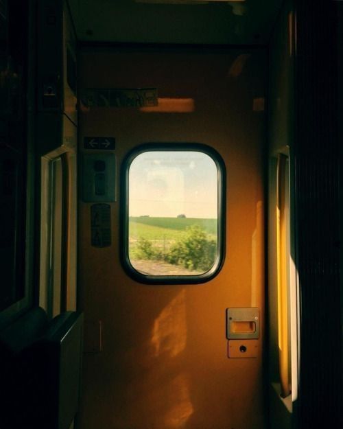 an open door on a train with the view out it's window at green fields