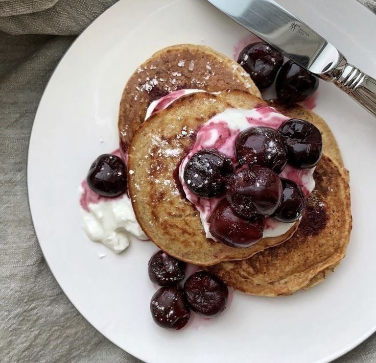 two pancakes with blueberries and whipped cream are on a white plate