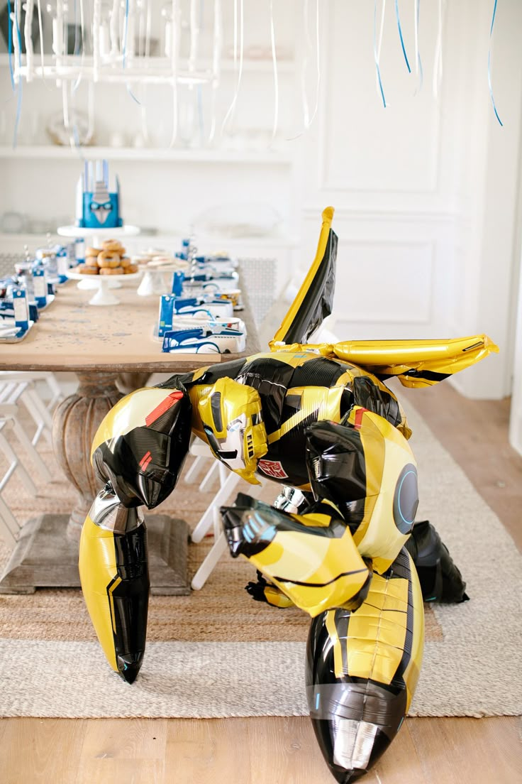 a yellow and black robot sitting on top of a wooden floor next to a table