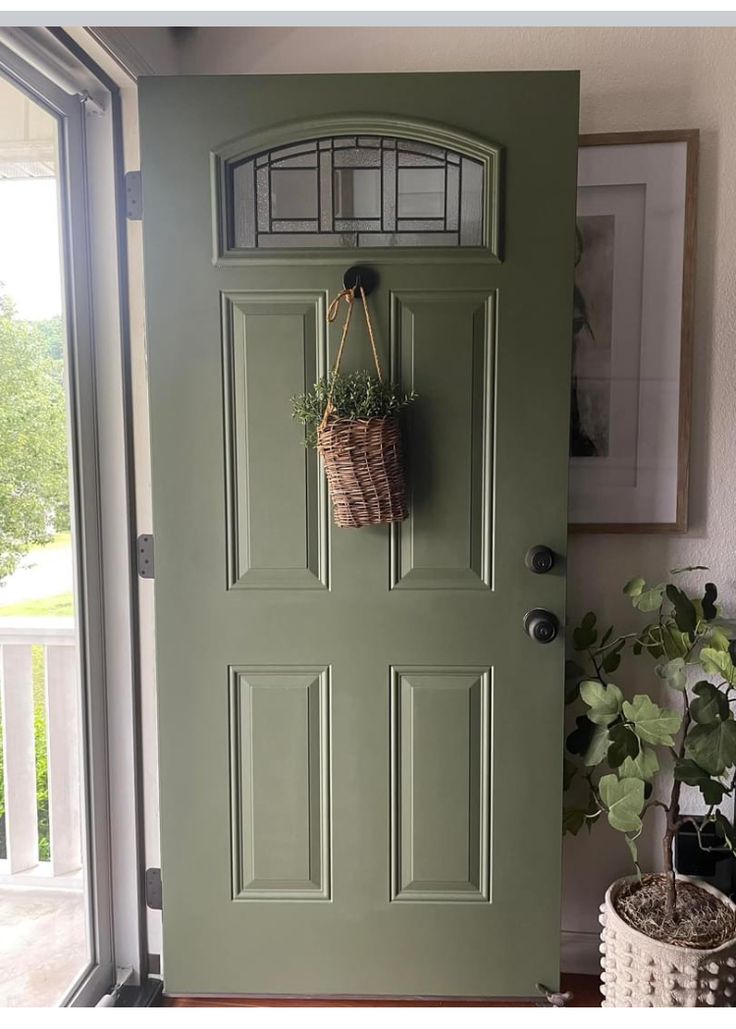 a green door with a basket hanging on it's side and a potted plant next to it