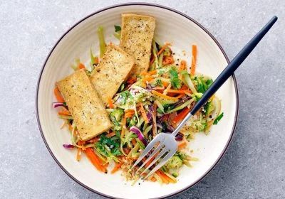 a white bowl filled with salad and two pieces of tofu on top of it