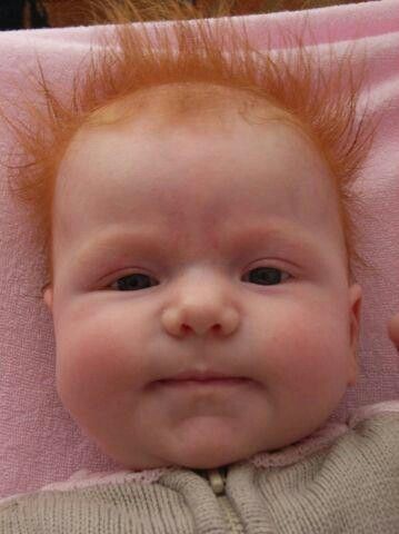 a baby with red hair laying on top of a pink blanket