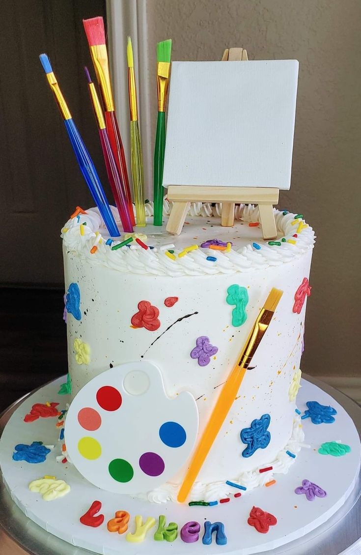 a birthday cake decorated with an easel and paintbrushes