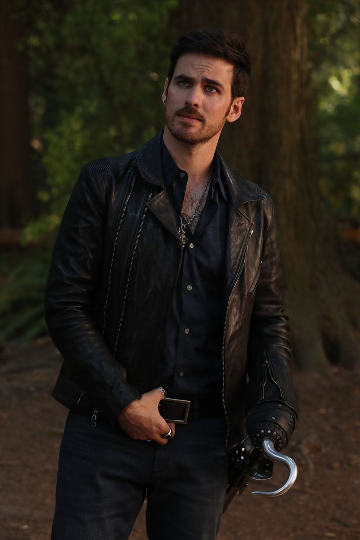 a man standing in the woods holding a white frisbee and wearing a leather jacket