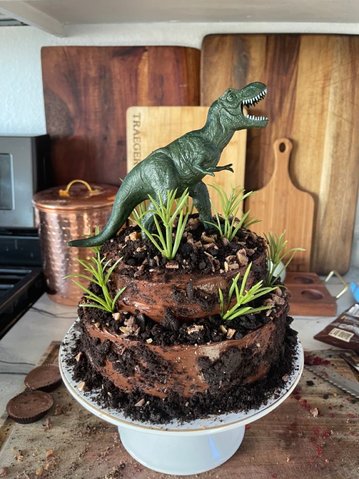 there is a cake that has a dinosaur on it and plants growing out of the top