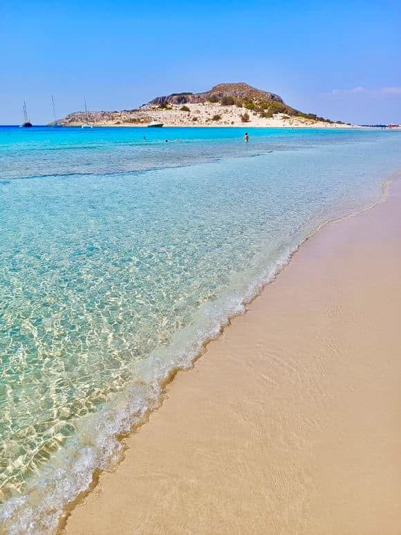 the water is crystal clear and blue at this beach near an island in the distance